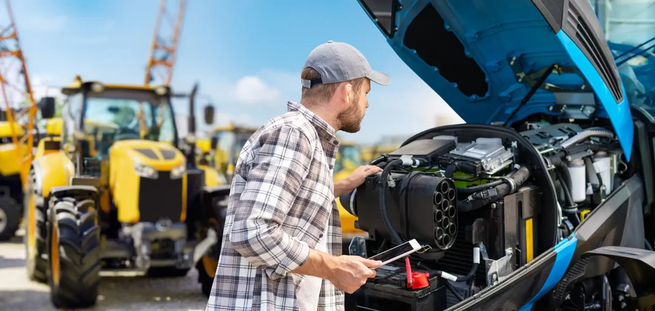 Man looking at the inside of a tractor engine whilst holding a tablet